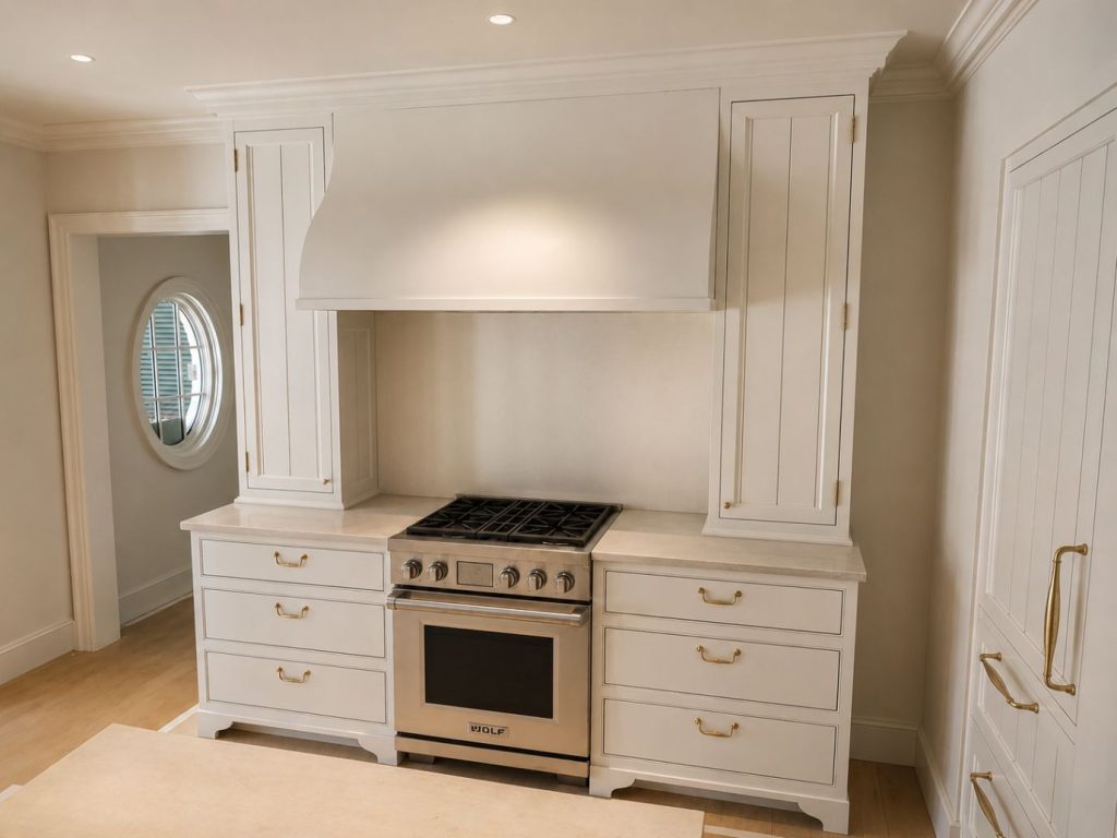 custom white range hood and cabinets and drawers surrounding a stainless steel range with sandstone counters.